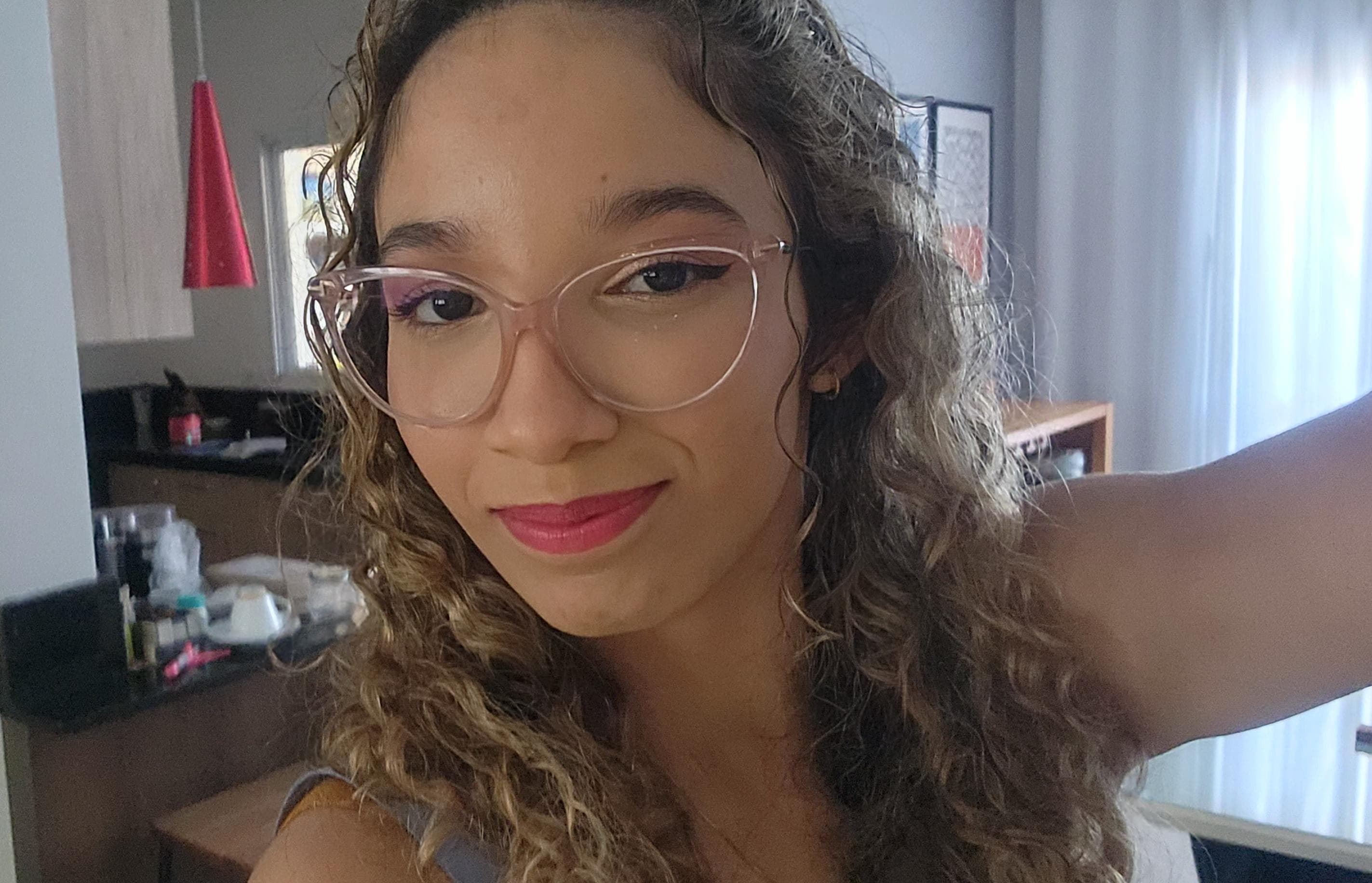 Foto da Heloísa: Mulher jovem usando óculos com camiseta branca e coque